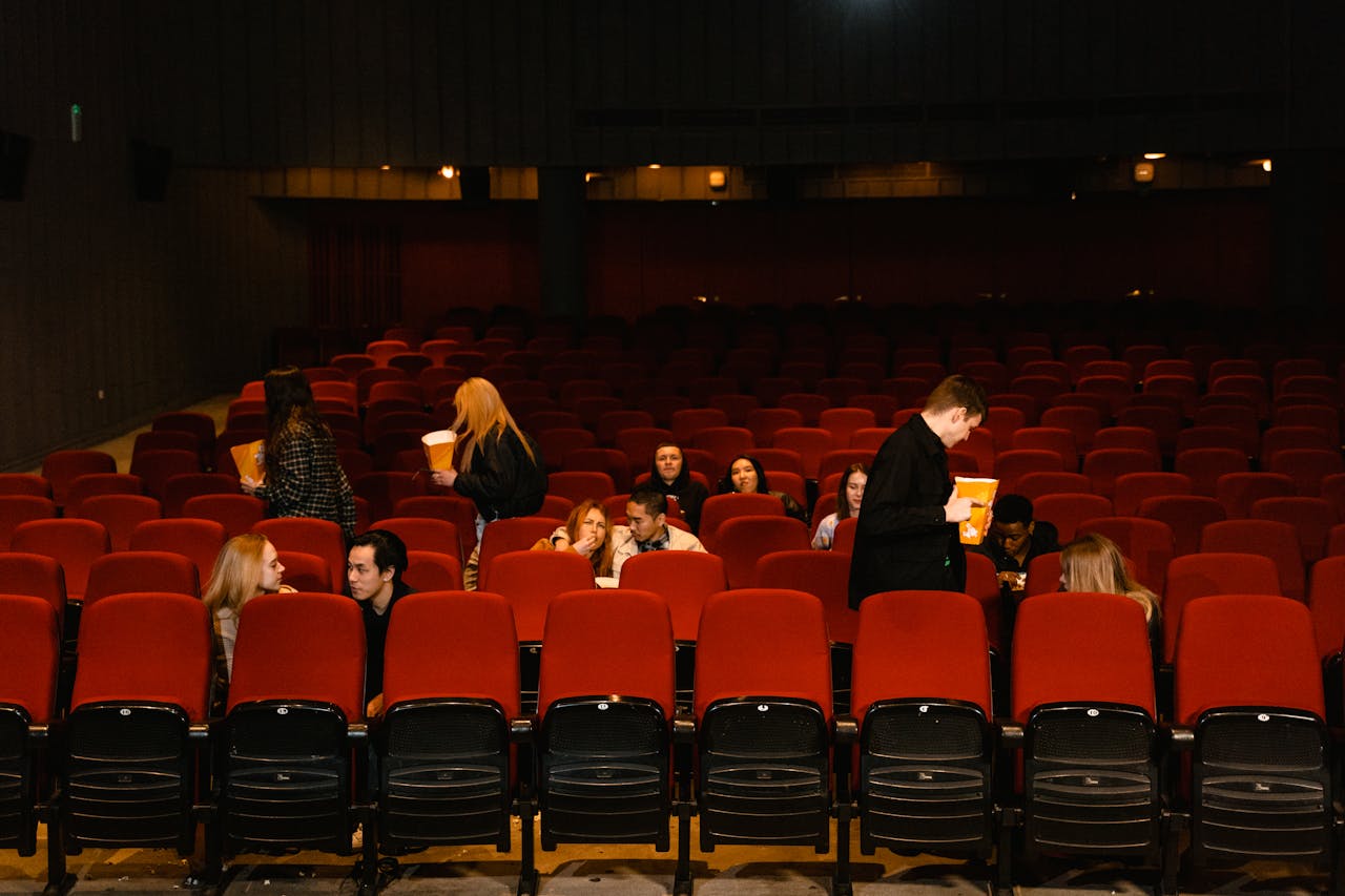 about-us-01 Group of people enjoying a movie with snacks in a cinema with red seats.